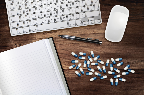 Medikamentenkapseln, Notizbuch, Kugelschreiber, Computertastatur und Computermaus auf Holztisch